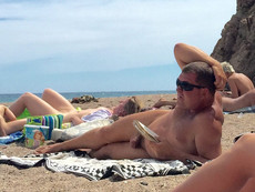 An elderly nudist sunbathes and reads a book on