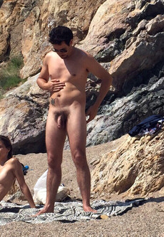 Naked guy sunbathing and bored on the beach